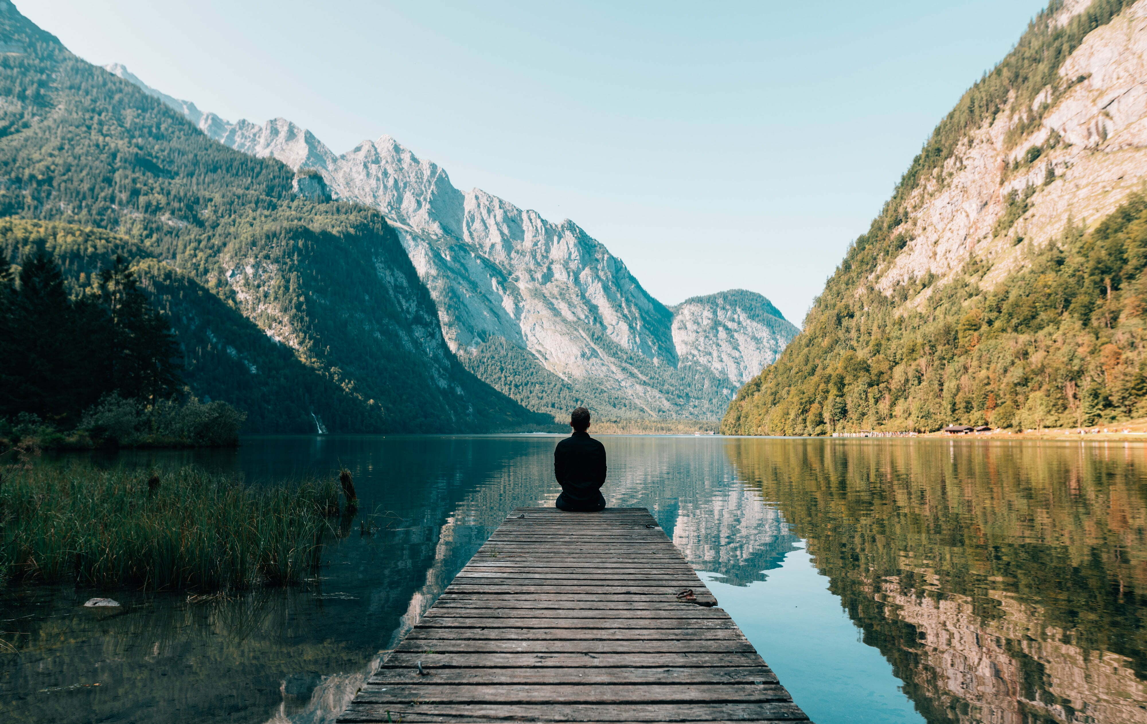 man sitting on dock looking at water and mountains